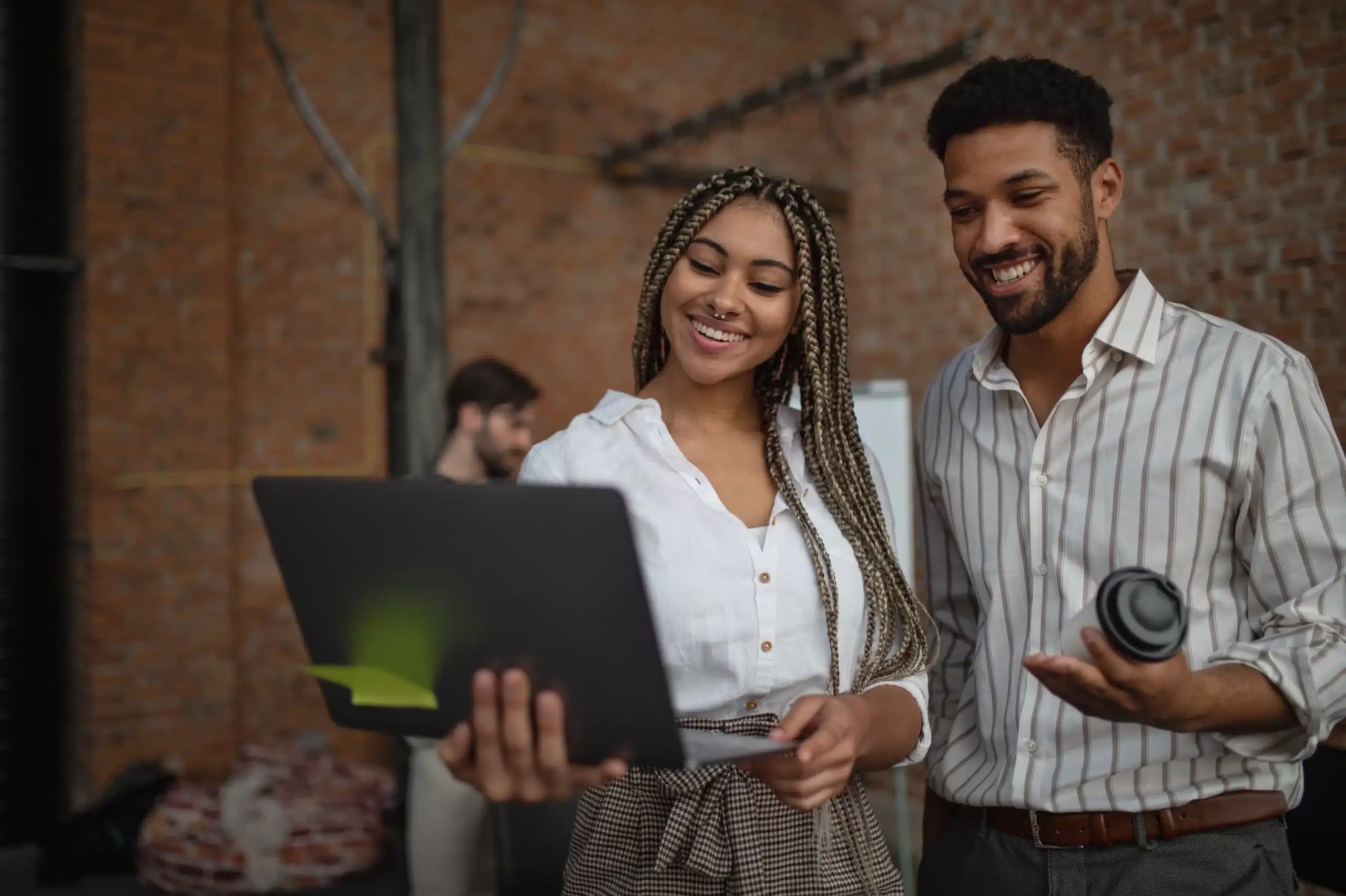 Jeune femme et homme d’affaires collaborant devant un ordinateur, souriants, en train de travailler dans l’IA en environnement startup.